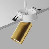 The Focus S Single Recessed Spotlight in matte gold with a white mounting fixture is installed on the ceiling, revealing wires and clips against a plain gray background, highlighting the stylish blend of recessed lighting elements.