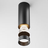 The Focus LED Fixed Round Surface Mounted Downlight 12W 3000K in black features a modern cylindrical design with a suspended inner bulb and decorative accents on a white background, offering an energy-efficient option for sleek contemporary lighting solutions.