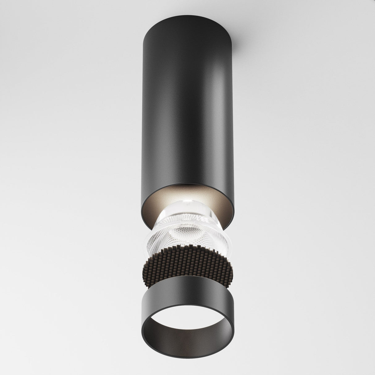 The Focus LED Dimmable Fixed Round Downlight 12W 4000K in black is a modern cylindrical surface-mounted light on a plain white ceiling. It features a transparent middle section revealing internal components, and a black ring at the base, enhancing its dimmable lighting capabilities.