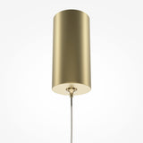 The Pro Base LED Thin Pendant Light - Gold, featuring a cylindrical design and brushed gold finish, hangs from the ceiling. Its minimalistic style includes an integrated LED light source and a sleek supporting wire, all set against a plain white background.