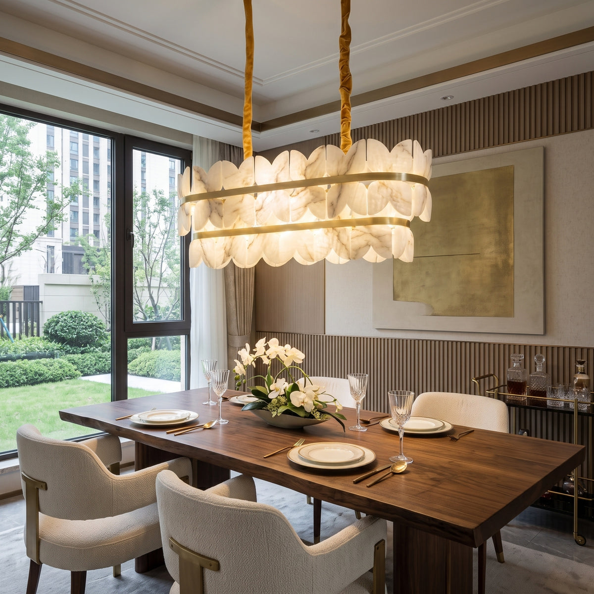 Petraia Linear Alabaster Chandelier in brushed brass, illuminated above a dark wood dining table with layered alabaster panels and twin gold ceiling stems.