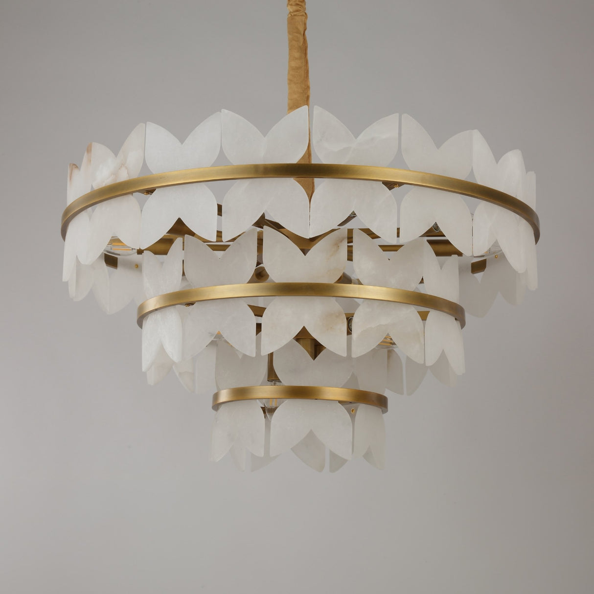 Niori Petraia three-tier chandelier with scalloped alabaster petals arranged around brushed brass rings, suspended from a fabric-covered chain.