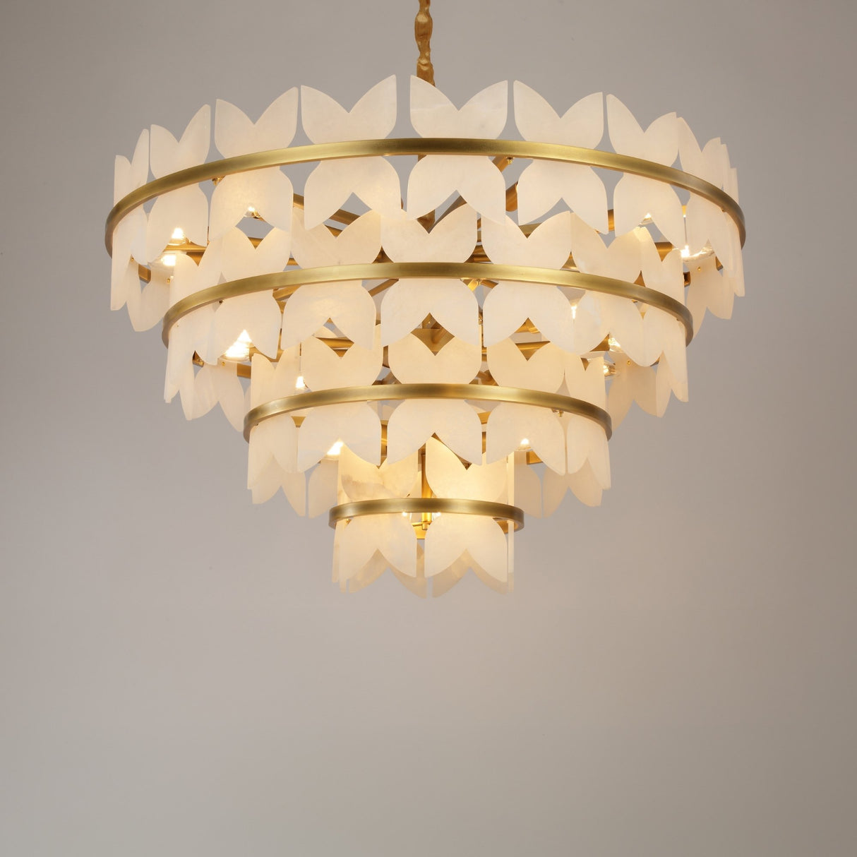 Niori Petraia four-tier floral chandelier with sculpted alabaster petals on brushed brass rings, suspended from a rope-wrapped drop against a light background.