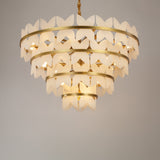Niori Petraia four-tier floral chandelier with sculpted alabaster petals on brushed brass rings, suspended from a rope-wrapped drop against a light background.