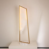 Niori Atria Small LED alabaster floor lamp with tapered illuminated panel in a brushed brass frame on a round white marble base, shown on a plinth.