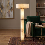 Colonnetta 3 Light Column Alabaster Floor Lamp with brushed brass collars and base disc, glowing beside a green armchair in a living room setting.