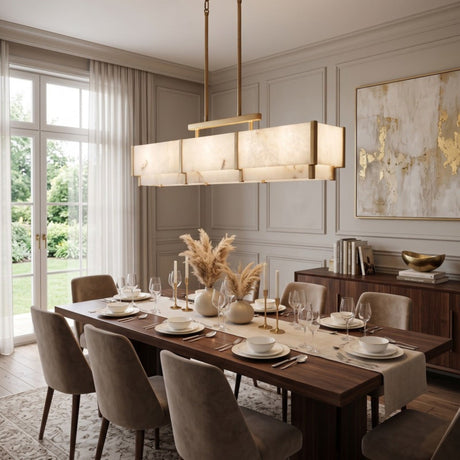 Quadrena Linear Alabaster Chandelier 113cm in Brushed Brass, glowing rectangular bar with two-tier stone-effect panels, shown above a dining table in a neutral-toned room.