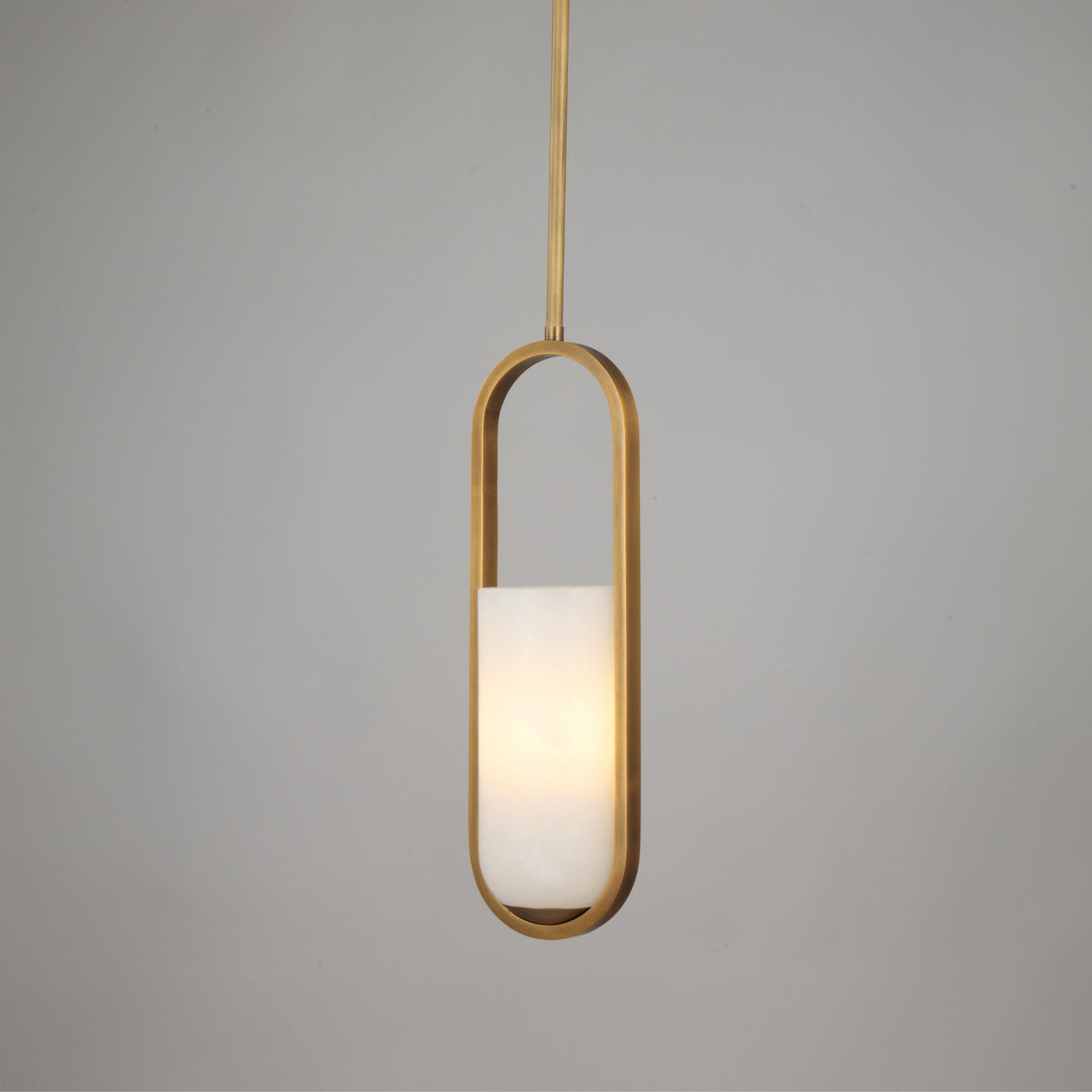 Niori Eliona Capsule pendant light featuring a natural alabaster cylinder in a brushed brass frame, suspended from a slim rod against light grey.