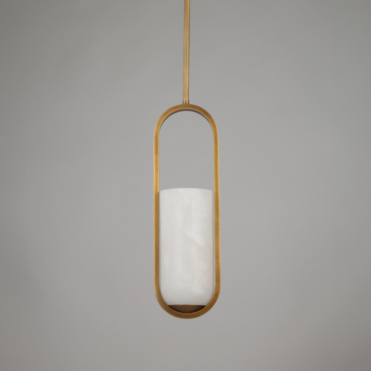 Eliona Capsule Alabaster Pendant Light in brushed brass with a vertical stone cylinder suspended inside a slim capsule frame on a light grey background.