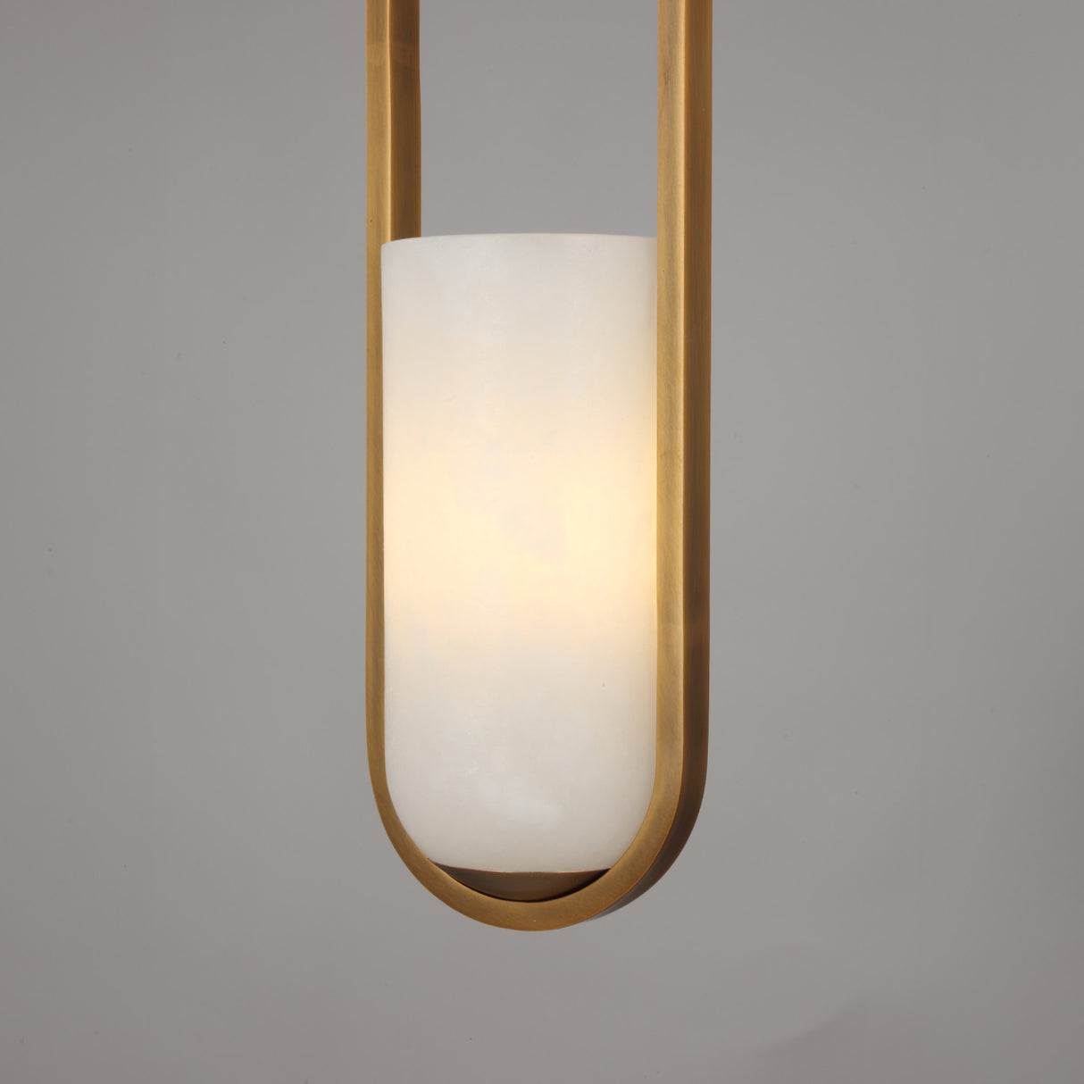 Niori Eliona Capsule pendant light with a natural Spanish alabaster cylinder shade suspended in a brushed brass loop frame, lit warm white.
