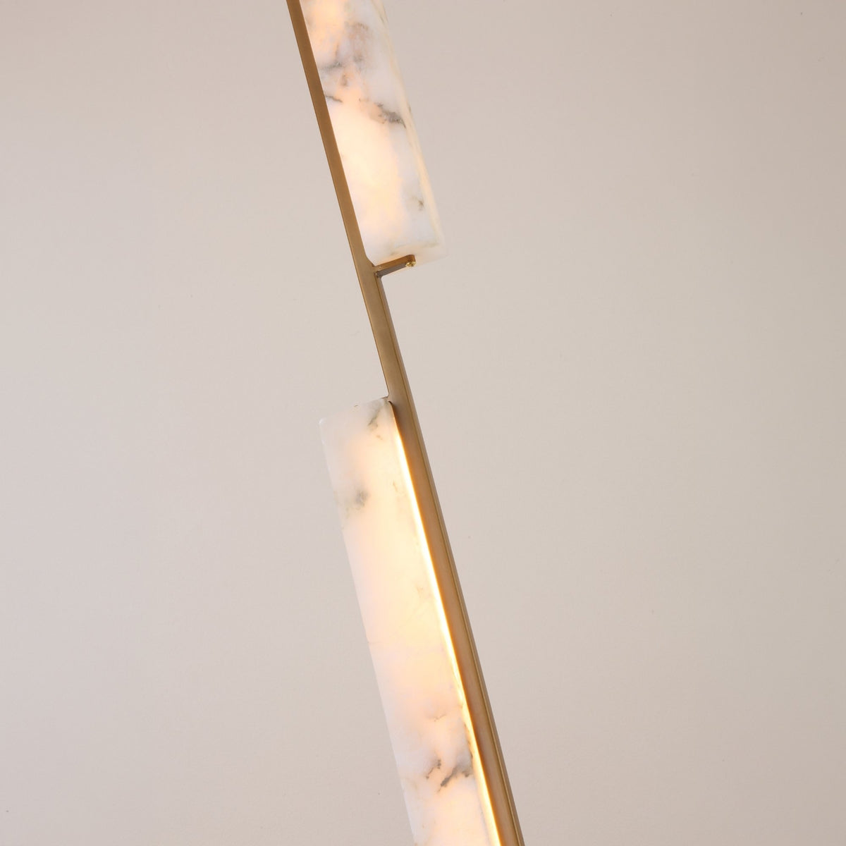 Close-up of Niori Selvara LED vertical duo pendant light showing staggered natural alabaster bars on a brushed brass stem, illuminated with warm white light.