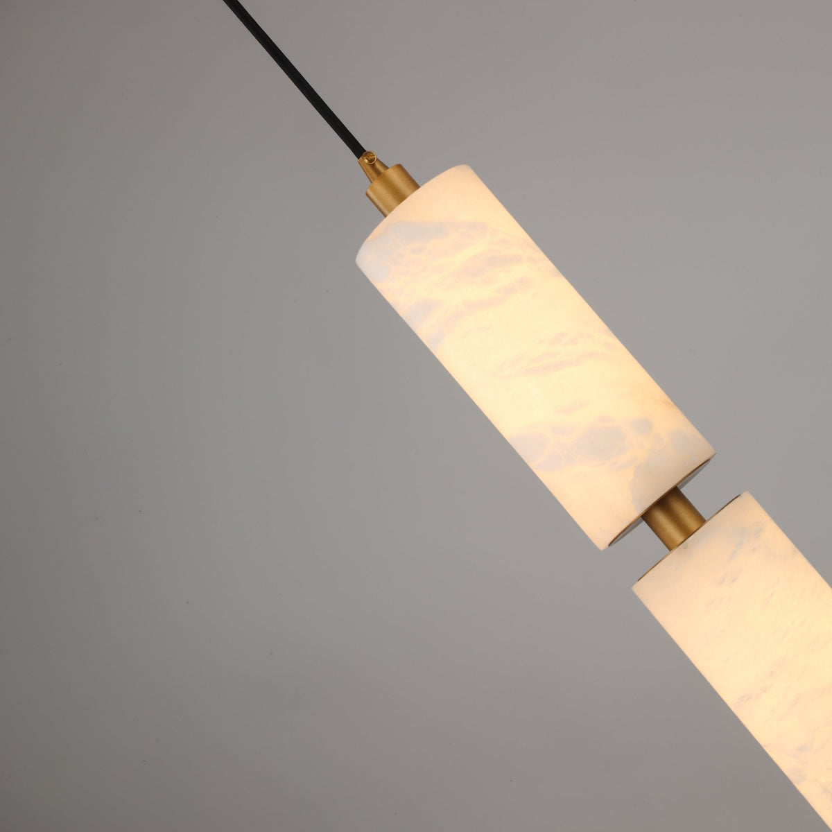 Niori Ardent Medium column pendant with stacked natural alabaster cylinders and brushed brass collar, suspended on a black cable against a grey background.