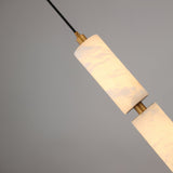 Niori Ardent Medium column pendant with stacked natural alabaster cylinders and brushed brass collar, suspended on a black cable against a grey background.