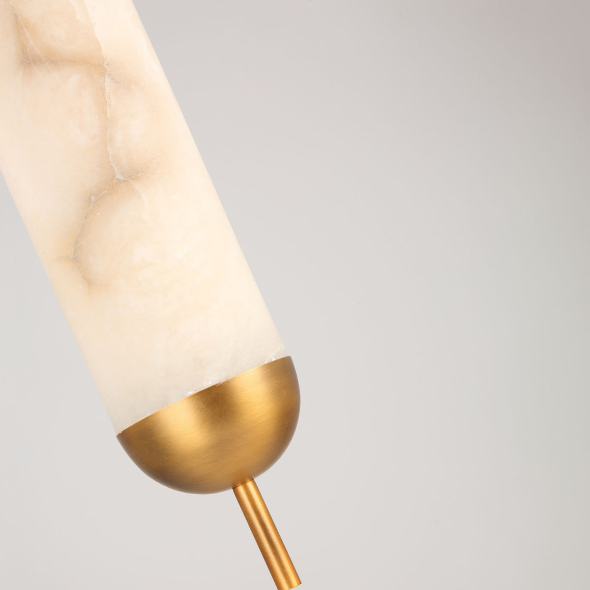 Close-up of the Zerith LED alabaster tube pendant light with domed brushed brass end cap and rod, shown against a plain light grey background.