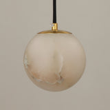 Lyvane extra small alabaster globe pendant light with brushed brass cap and black fabric cable, natural stone veining, on a plain light background.