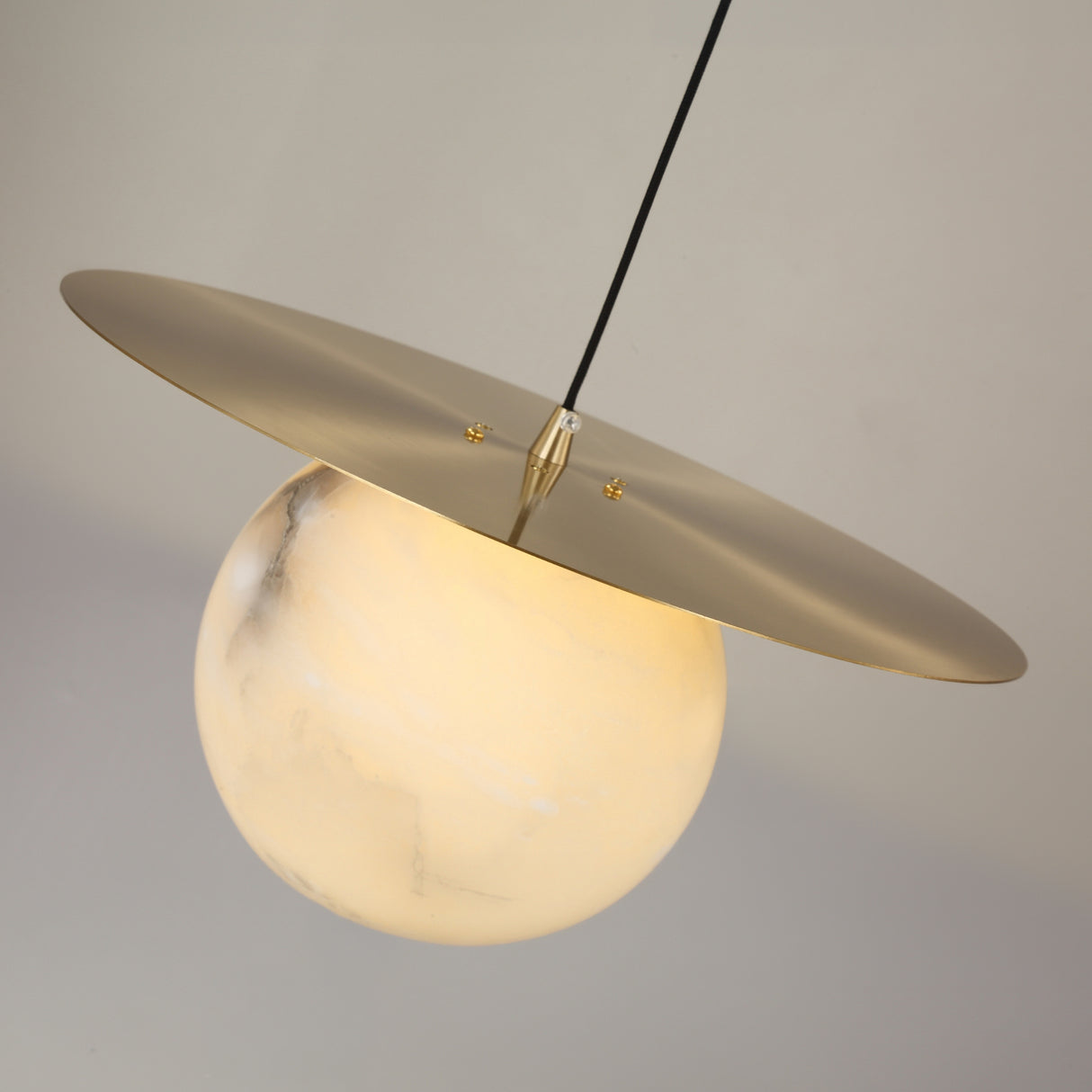 Marenzo Small Orb Alabaster Pendant Light in brushed brass, featuring a glowing alabaster sphere beneath a flat brass disc, shown against a plain light grey background.