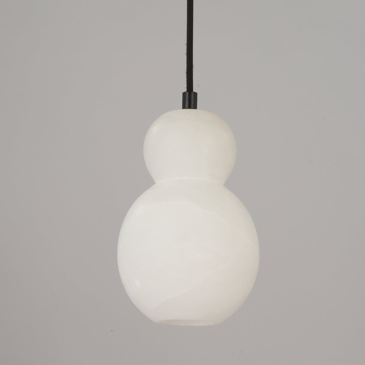 Orlune sculpted pear alabaster pendant light in soft white by Niori, with double-gourd form on a black cord against a plain grey background.