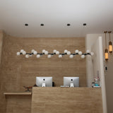 Niori Axis 27 Light Alabaster Linear Chandelier in matte black suspended above a travertine reception desk with iMacs and brass alabaster wall lights.