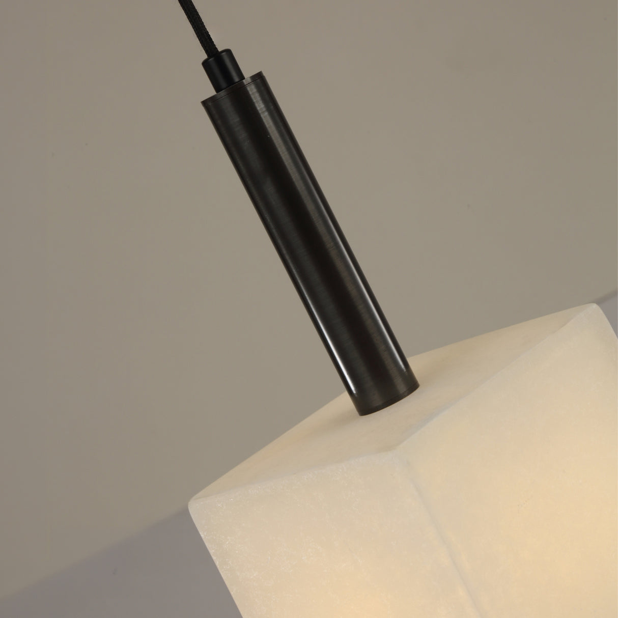 Close-up of the Draxen alabaster drum pendant light, showing the faceted alabaster shade meeting a matte black cylindrical stem with brushed brass collar, on a plain neutral background.