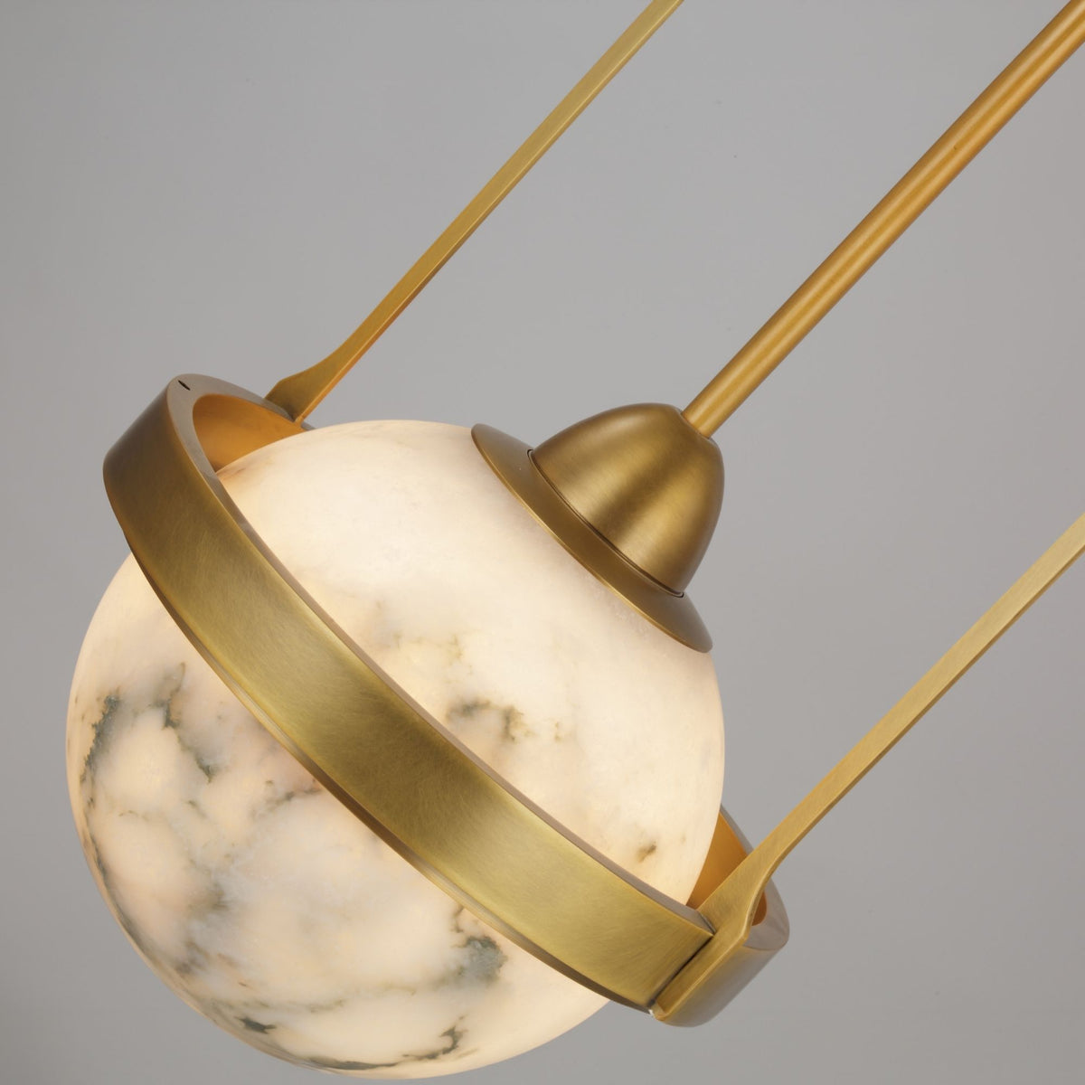 Calis Alabaster Single Pendant Light in Brushed Brass, close-up of the spherical alabaster globe held by an arched brass band and stem.