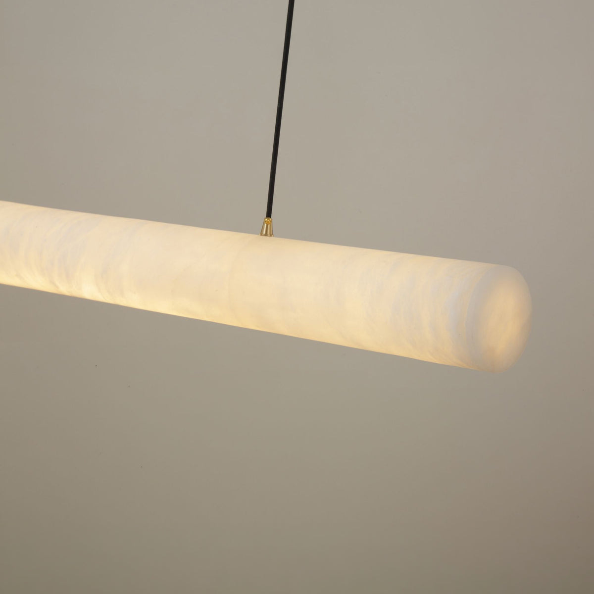 Zareon LED Large Linear Alabaster Chandelier in soft white, a cylindrical stone pendant glowing warm white, suspended on a black cable against a plain light grey background.