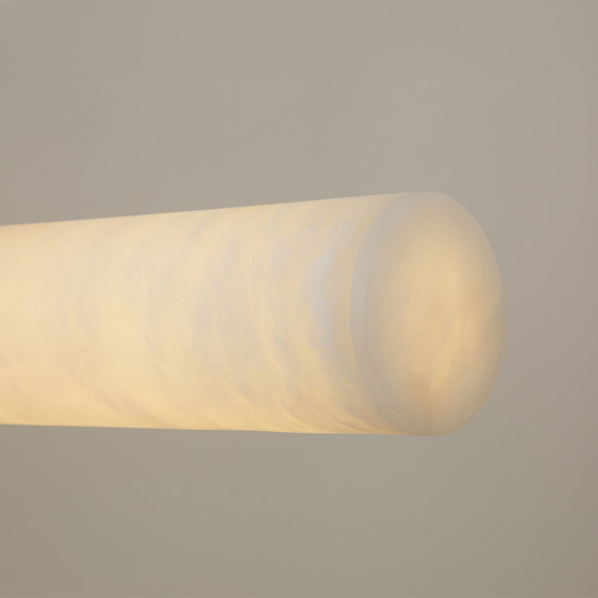 Close-up of the Zareon Small alabaster chandelier's cylindrical arm, showing natural stone texture glowing warm white, set against a plain grey background.
