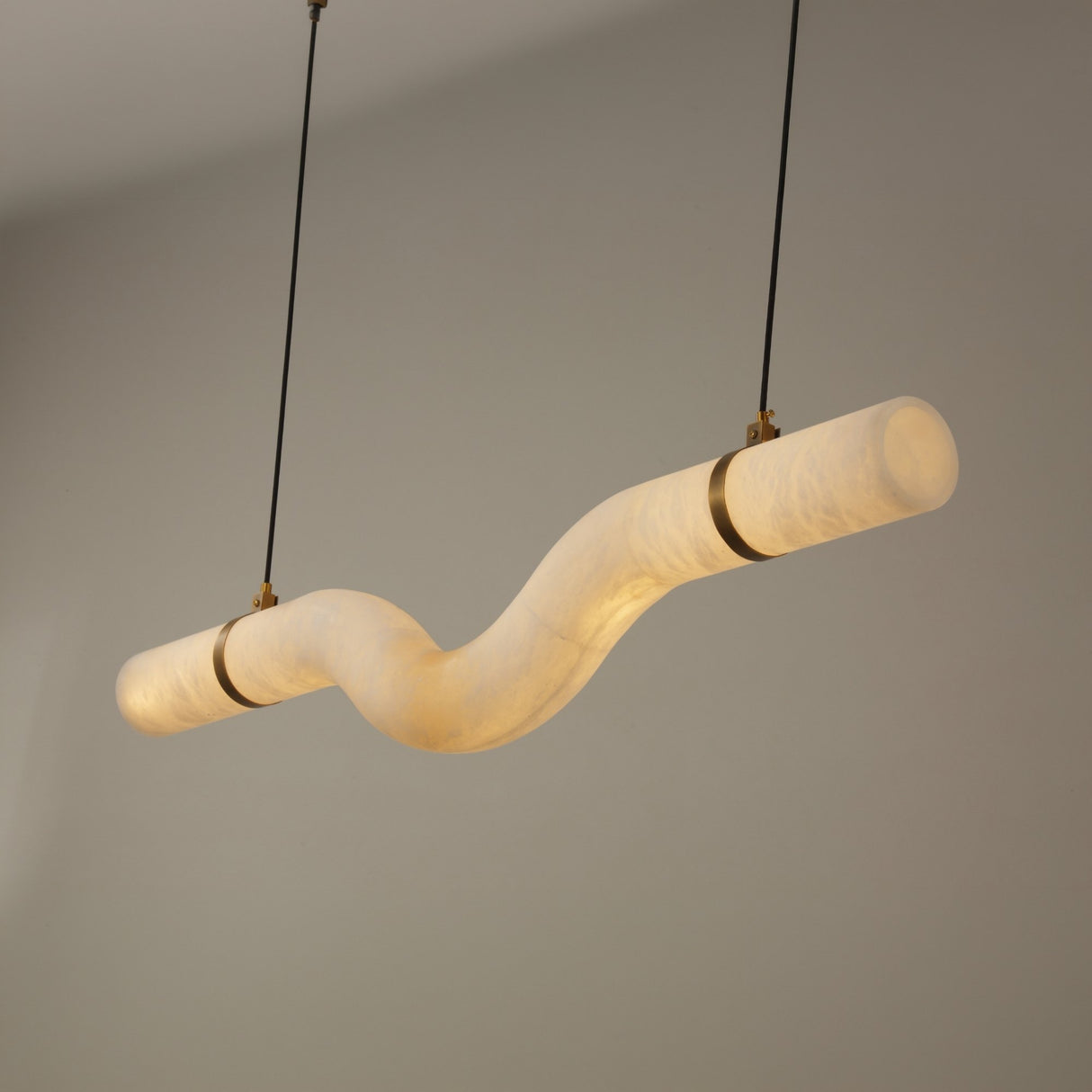 Niori Zareon Small curved alabaster LED chandelier in soft white with brushed brass cradles, suspended horizontally on slim cables against a neutral background.