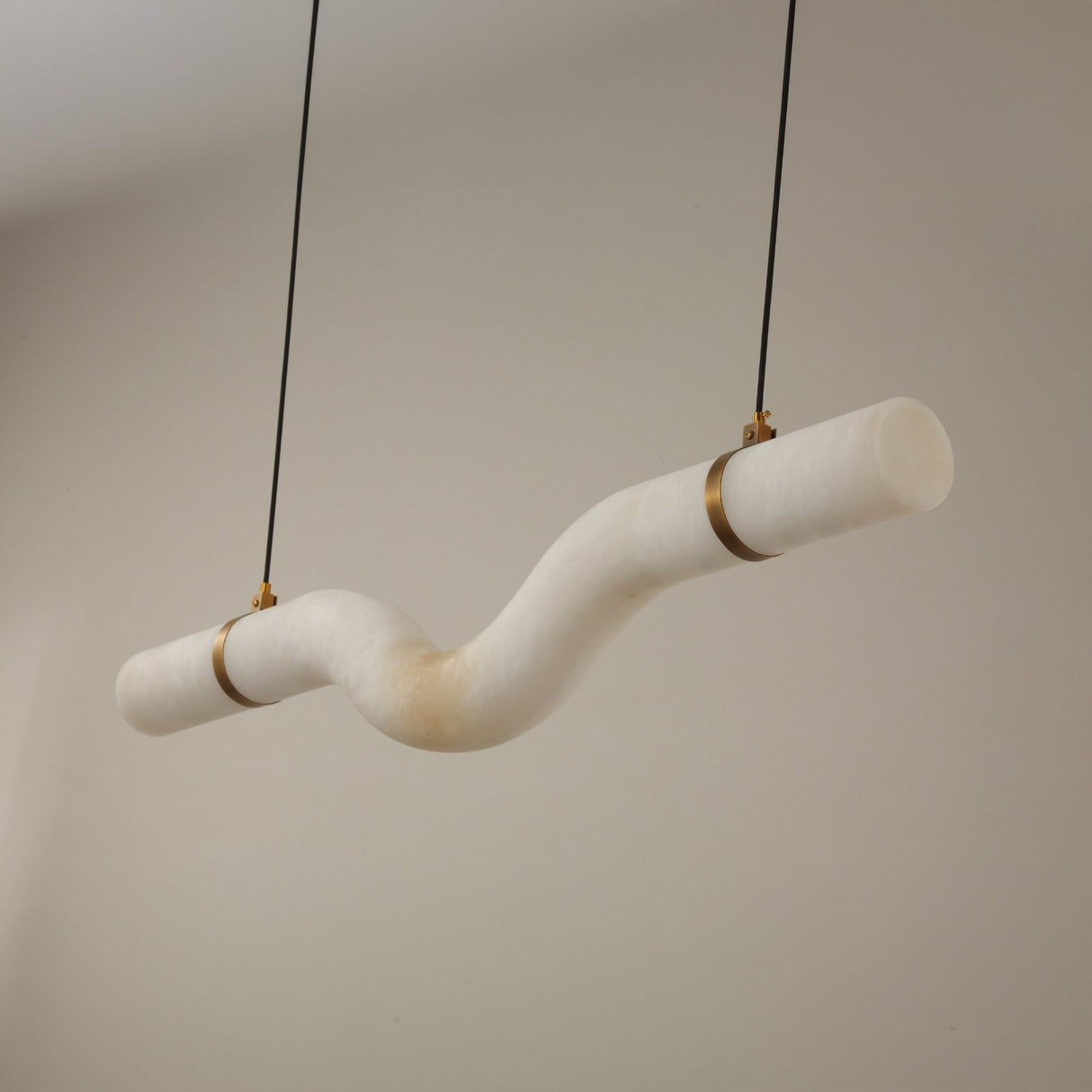 Niori Zareon Small curved alabaster chandelier with an S-shaped horizontal profile, brushed brass cradles and cables, shown against a neutral background.