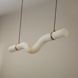 Niori Zareon Small curved alabaster chandelier with an S-shaped horizontal profile, brushed brass cradles and cables, shown against a neutral background.