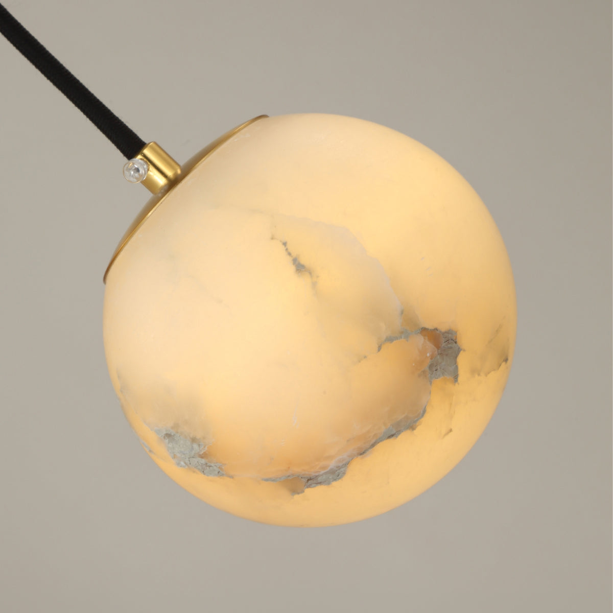 Lyvane extra small alabaster globe pendant light with brushed brass cap and black fabric cable, shown against a plain grey background.