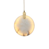 Niori Luna 200mm alabaster disc pendant light illuminated warm white, with brushed brass hinge and slim suspension cable, shown on a plain white background.