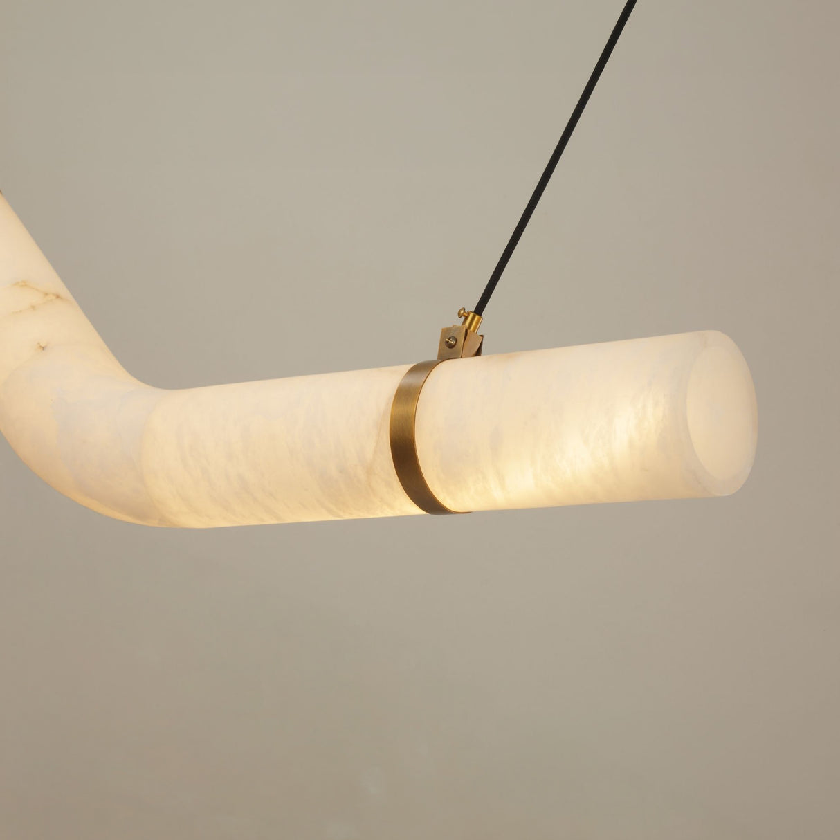 Close-up of the Zareon Small alabaster chandelier's angled joint, showing a brushed brass cuff securing the glowing white alabaster cylinders, suspended by black cables.