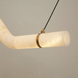 Close-up of the Zareon Small alabaster chandelier's angled joint, showing a brushed brass cuff securing the glowing white alabaster cylinders, suspended by black cables.