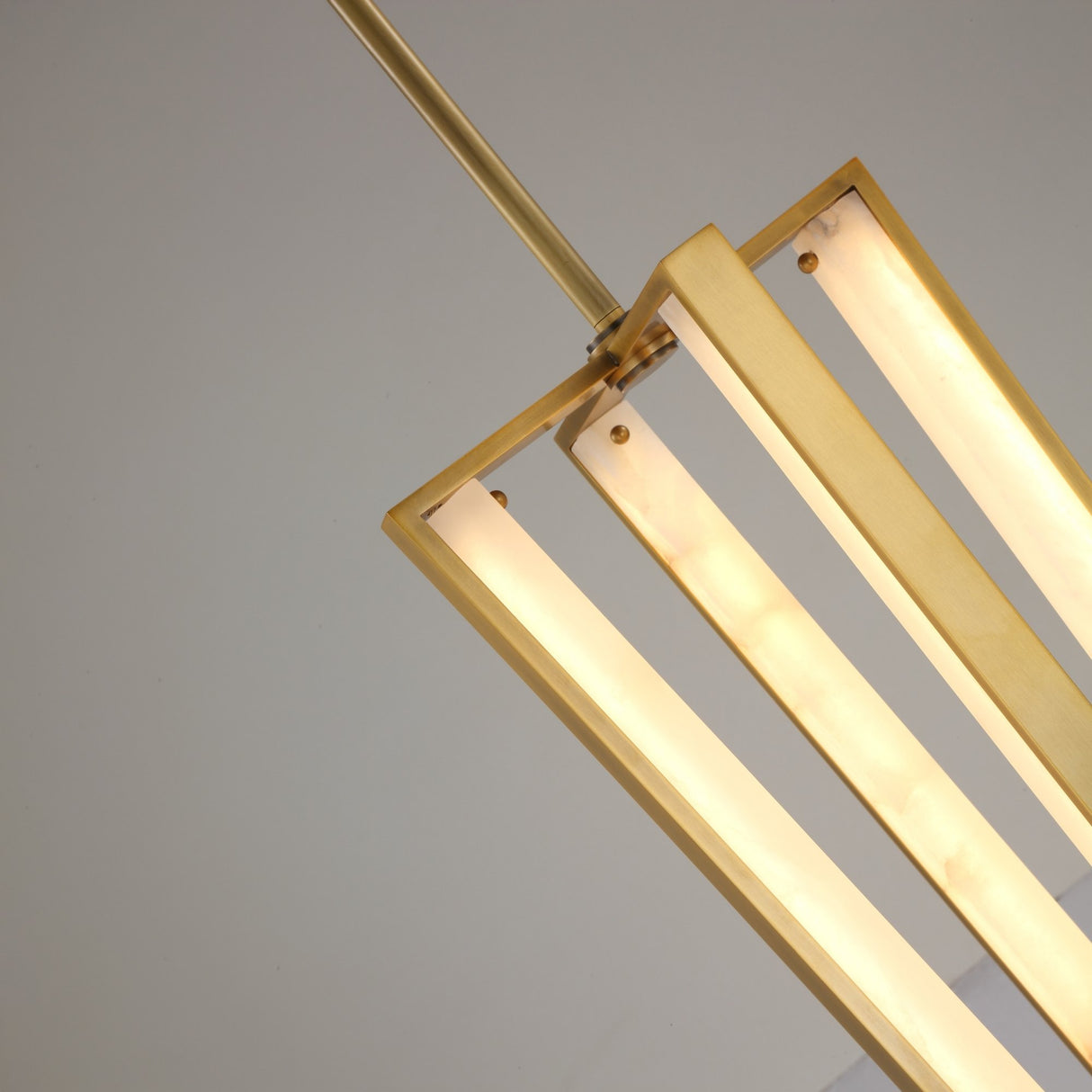 Close-up of the Niori Elvaris LED pendant light showing brushed brass frame, alabaster bars glowing warm white, and slim drop rod against a pale background.