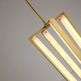 Close-up of the Niori Elvaris LED pendant light showing brushed brass frame, alabaster bars glowing warm white, and slim drop rod against a pale background.