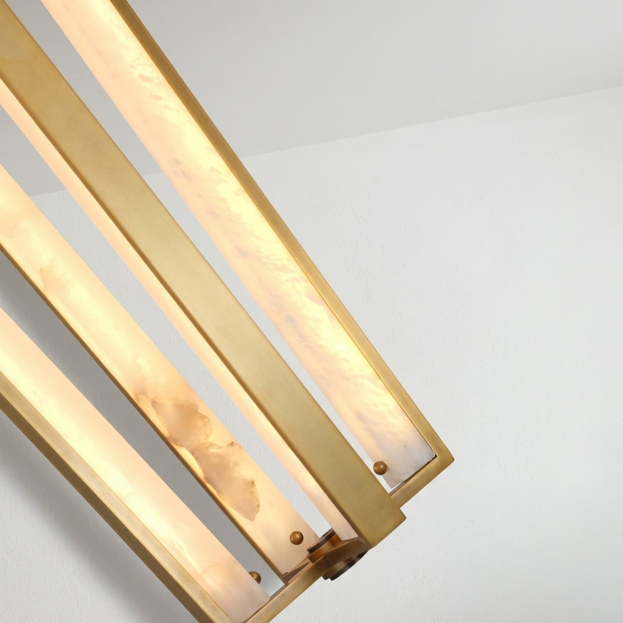 Close-up of Niori Elvaris LED pendant light showing tapered brushed brass cage with vertical alabaster bars glowing warm white against a plain ceiling.