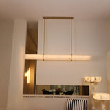 Niori Zarune LED linear alabaster chandelier in brushed brass, suspended from an oval canopy by two slim rods in a contemporary showroom setting.