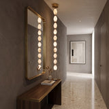 Brisalda 10 Light Faceted Alabaster Pendant Light in brushed brass, vertical stack of hexagonal stones with brass spheres, shown beside a matching mirror in a hallway.