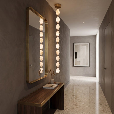 Brisalda 10 Light Faceted Alabaster Pendant Light in brushed brass, vertical stack of hexagonal stones with brass spheres, shown beside a matching mirror in a hallway.