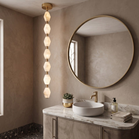 Brisalda 7 Light Faceted Alabaster Pendant Light in Brushed Brass, vertical drop of hexagonal alabaster stones with brass spheres, shown above a bathroom vanity with round mirror.