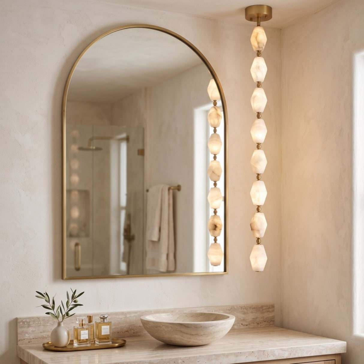 Brisalda 8 Light Faceted Alabaster Pendant Light in Brushed Brass, vertical drop of hexagonal alabaster stones with brass ceiling canopy, shown beside an arched mirror in a bathroom.