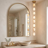 Brisalda 8 Light Faceted Alabaster Pendant Light in Brushed Brass, vertical drop of hexagonal alabaster stones with brass ceiling canopy, shown beside an arched mirror in a bathroom.