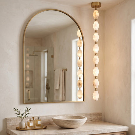 Brisalda 8 Light Faceted Alabaster Pendant Light in Brushed Brass, vertical drop of hexagonal alabaster stones with brass ceiling canopy, shown beside an arched mirror in a bathroom.