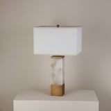 Ravelle table lamp with fluted alabaster column, brushed brass cap and base, and rectangular soft white fabric shade on a plinth.