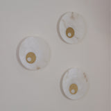 Three Selvana Small round alabaster wall lights with brushed brass centre bosses, mounted on a plain white wall.