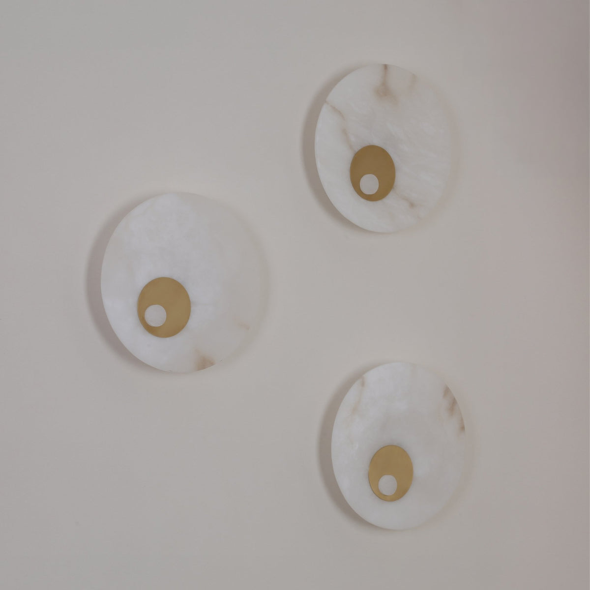 Three Selvana Large round alabaster wall lights with brushed brass centre details, integrated LED, mounted on a plain white wall.