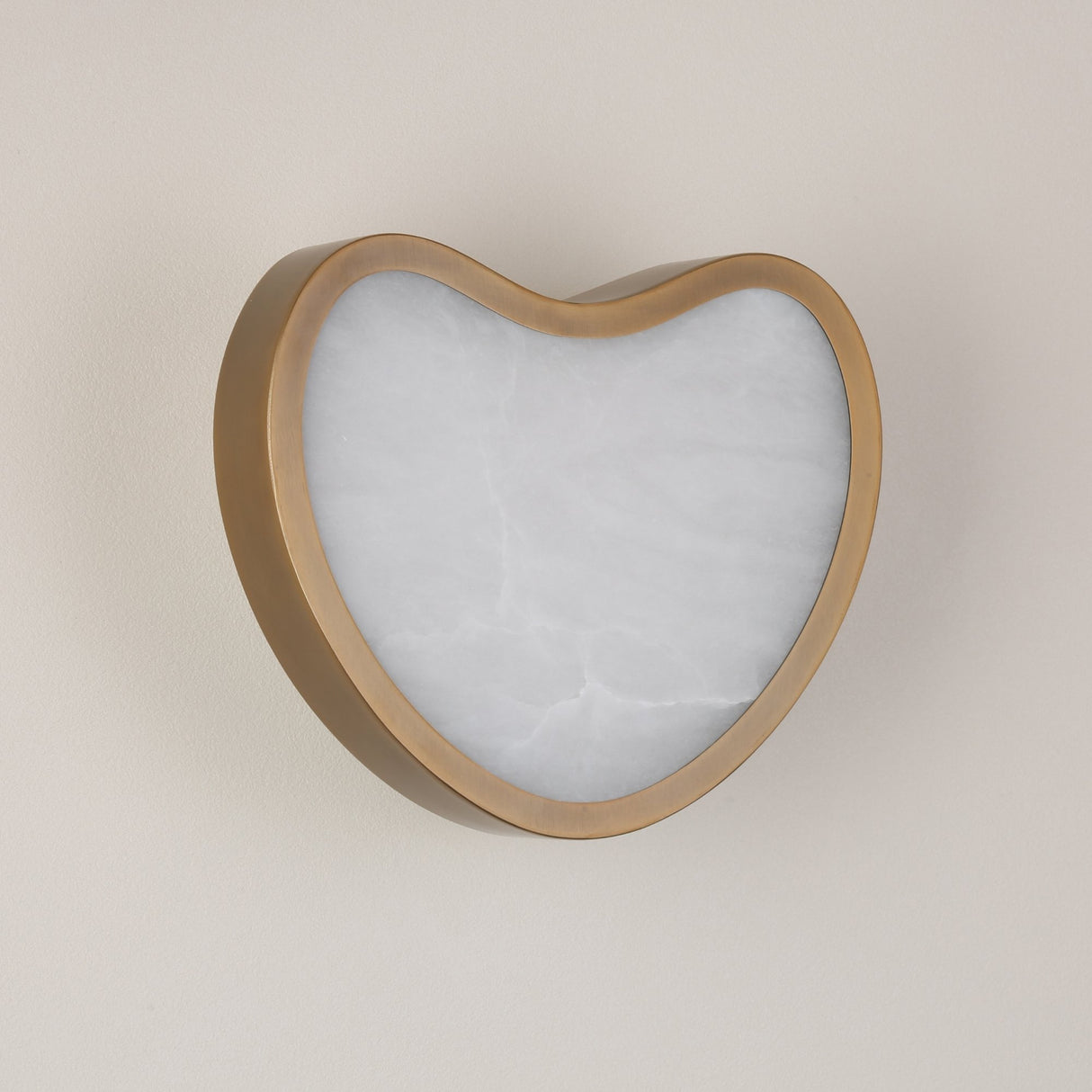 Niori Marea LED wall light with a curved brushed brass shell framing a heart-shaped natural alabaster face, mounted on a pale wall.
