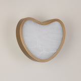 Niori Marea LED wall light with a curved brushed brass shell framing a heart-shaped natural alabaster face, mounted on a pale wall.