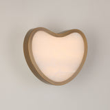Niori Marea LED wall light with a heart-shaped brushed brass shell framing a natural Spanish alabaster face, glowing warm white against a light grey wall.