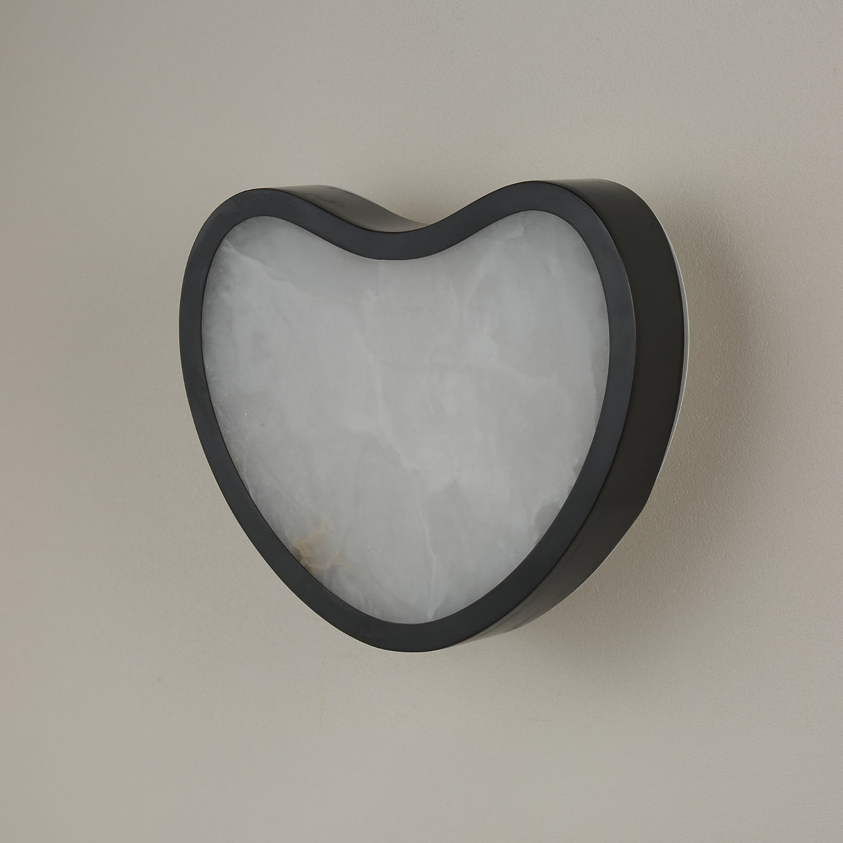 Niori Marea LED wall light with matte black copper frame wrapping a teardrop-shaped natural Spanish alabaster panel, shown against a pale wall.